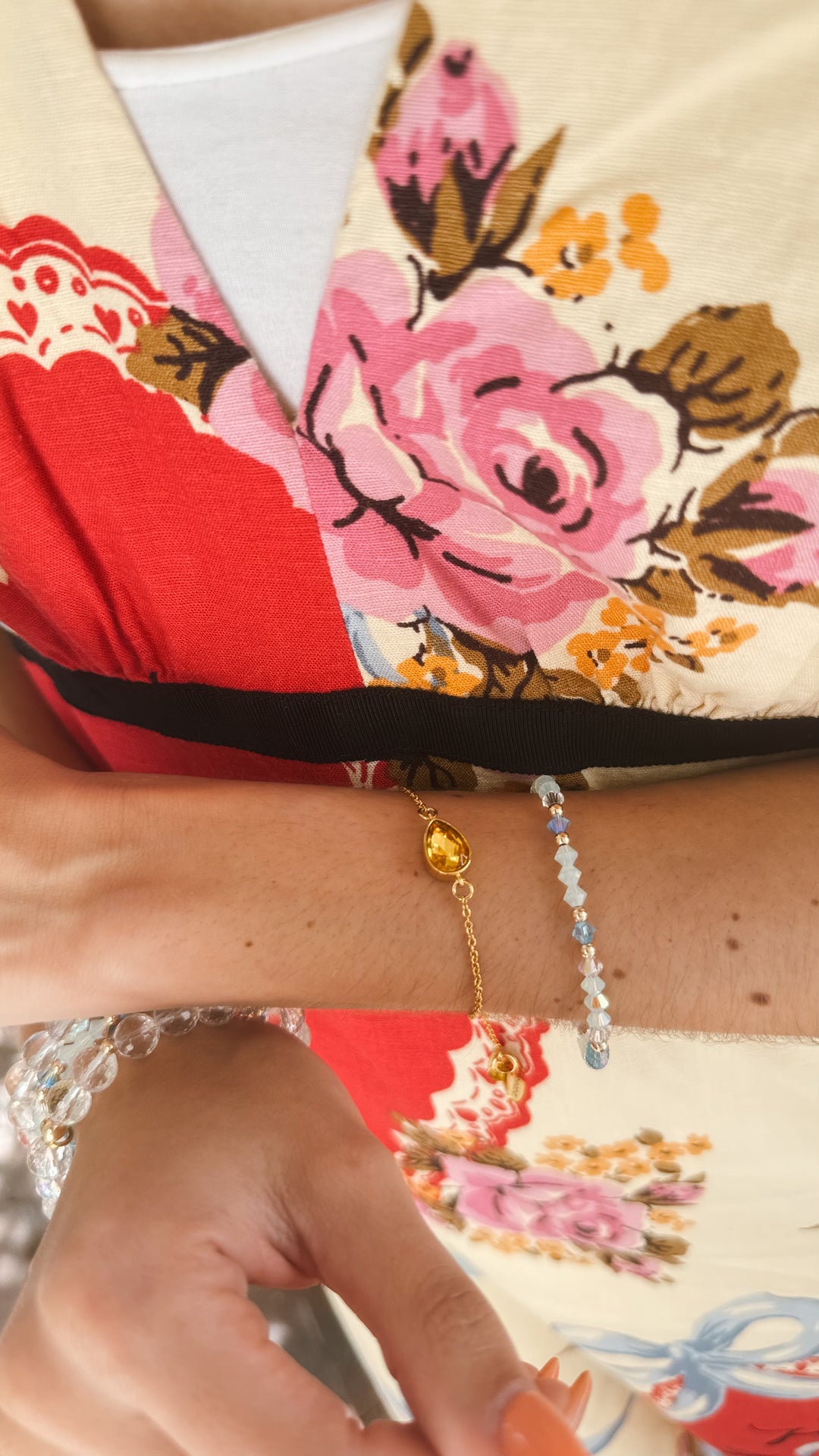Close-up of a dainty bracelet stack with citrine chain and aqua blue gemstones against a floral background