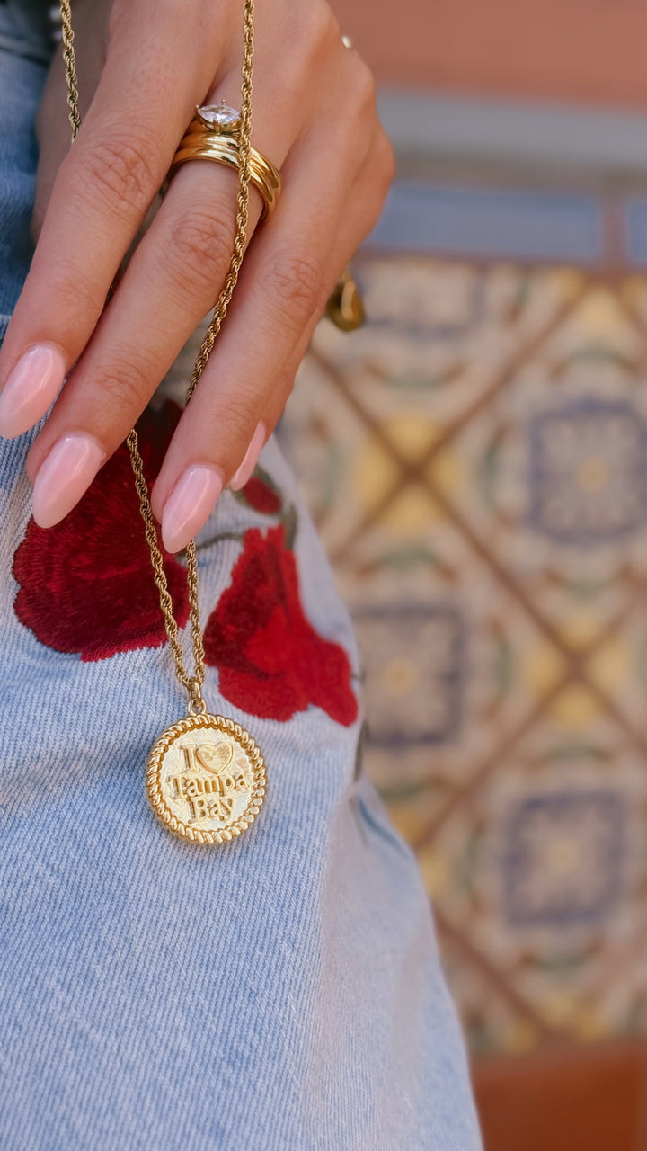 Gold necklace with a round pendant worn by a person against a colorful patterned background