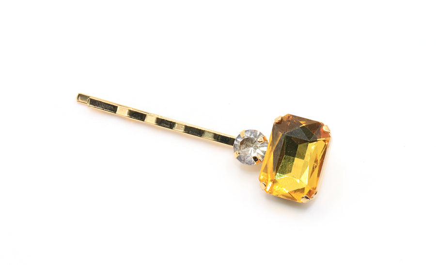 Hairpin with a large yellow gemstone and smaller clear gemstone on a white background